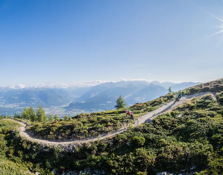 Ciclista di mountain bike salta su una rampa nel bike park Kronplatz – azione downhill in Valle Pusteria vicino a Kiens in Alto Adige